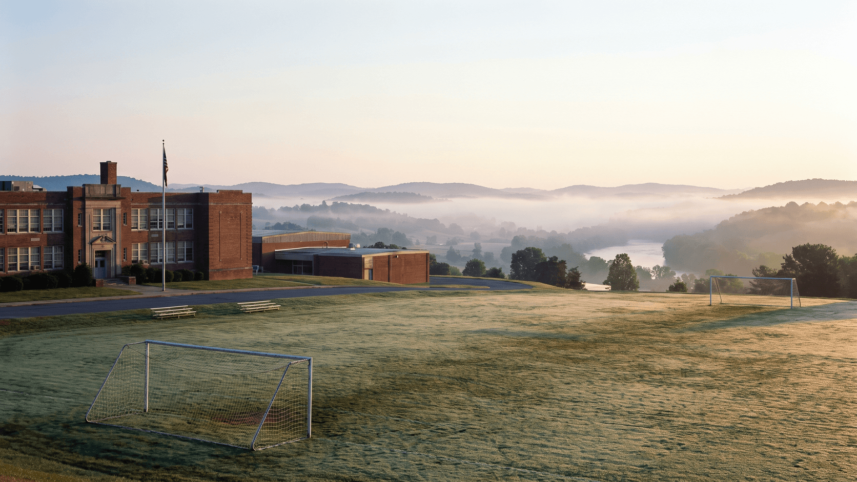 Rural high school practice field at dawn, rolling hills in mist