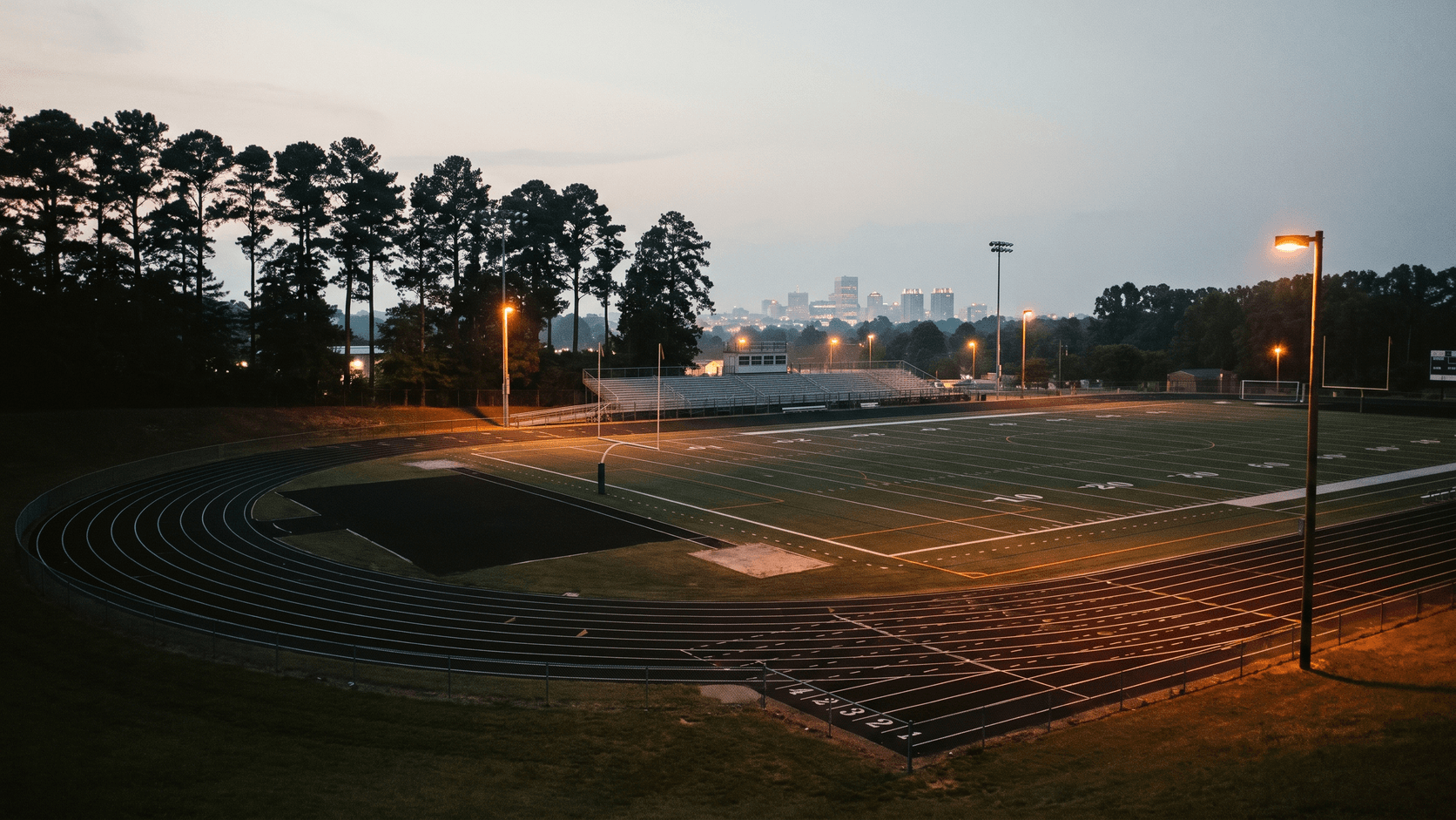 Suburban high school track and field at dusk, city glow on the horizon