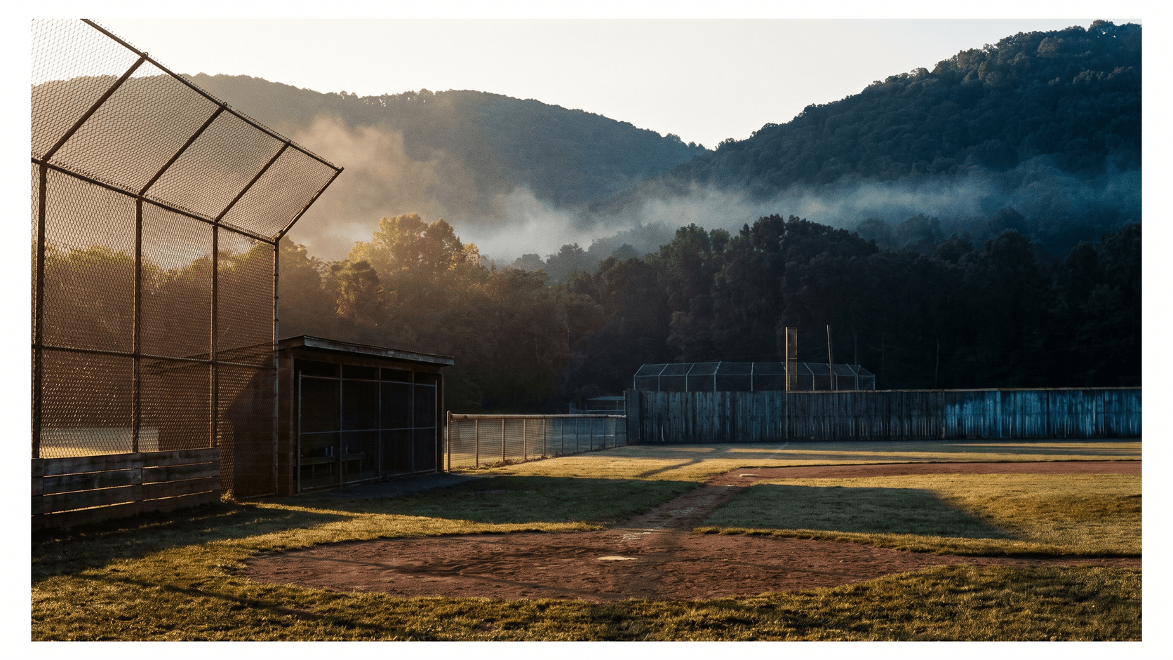 High school baseball field at golden hour with a wooded ridgeline behind the outfield