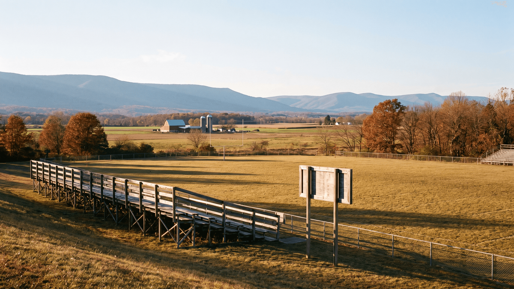 Small-town football field in autumn, farmland and mountain ridges beyond the end zone