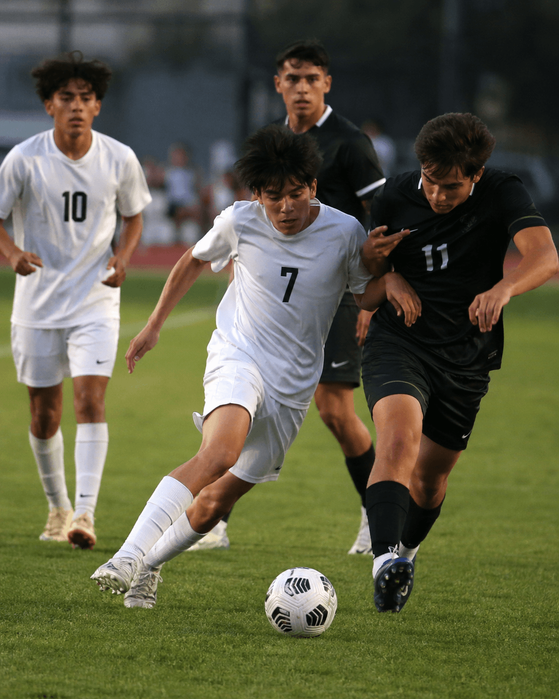 Boys high school soccer match: a midfielder in a Plus Effort-style white kit dribbling past a defender.